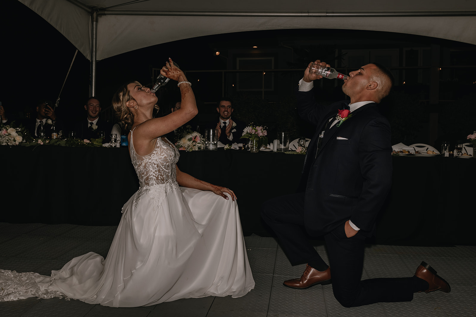 A playful moment at the reception as the bride and groom compete in a fun drinking contest, adding some lighthearted fun to their backyard wedding celebration