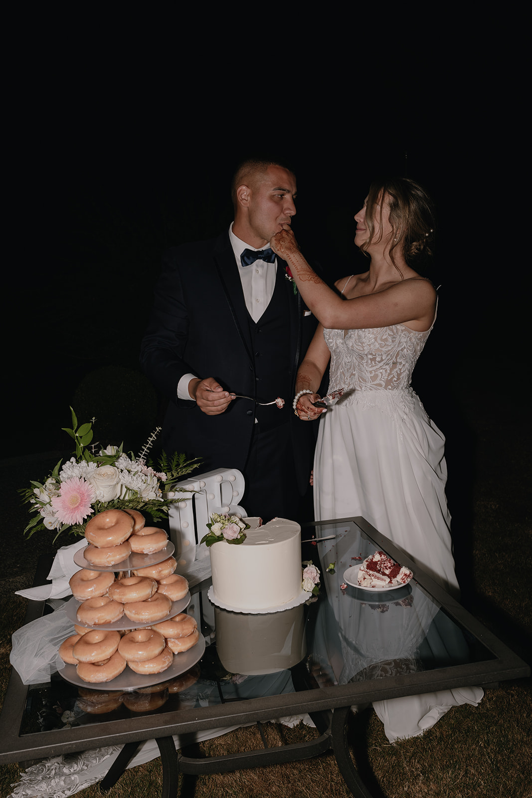 The bride lovingly feeds the groom cake during their backyard wedding reception, creating a joyful, fun-filled moment under the stars.