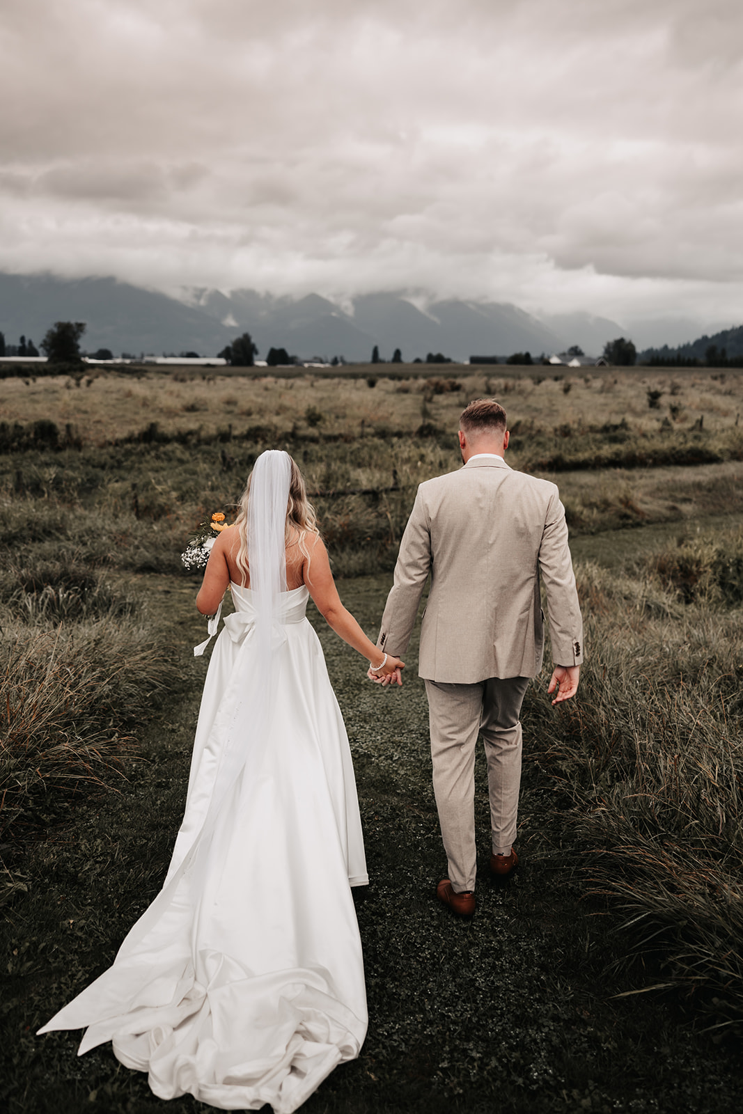 The newlyweds walk hand-in-hand across a lush field, leaving their ceremony with big smiles. The cloudy skies don’t diminish the joy of their stress-free wedding day.