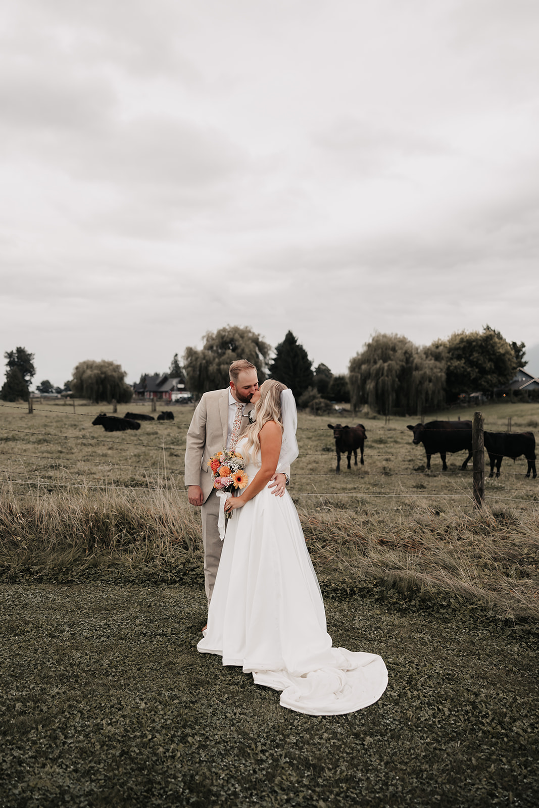 The couple shares a sweet kiss, with cows grazing behind them. Their laid-back, adventurous spirit embodies what a stress-free wedding day looks like.