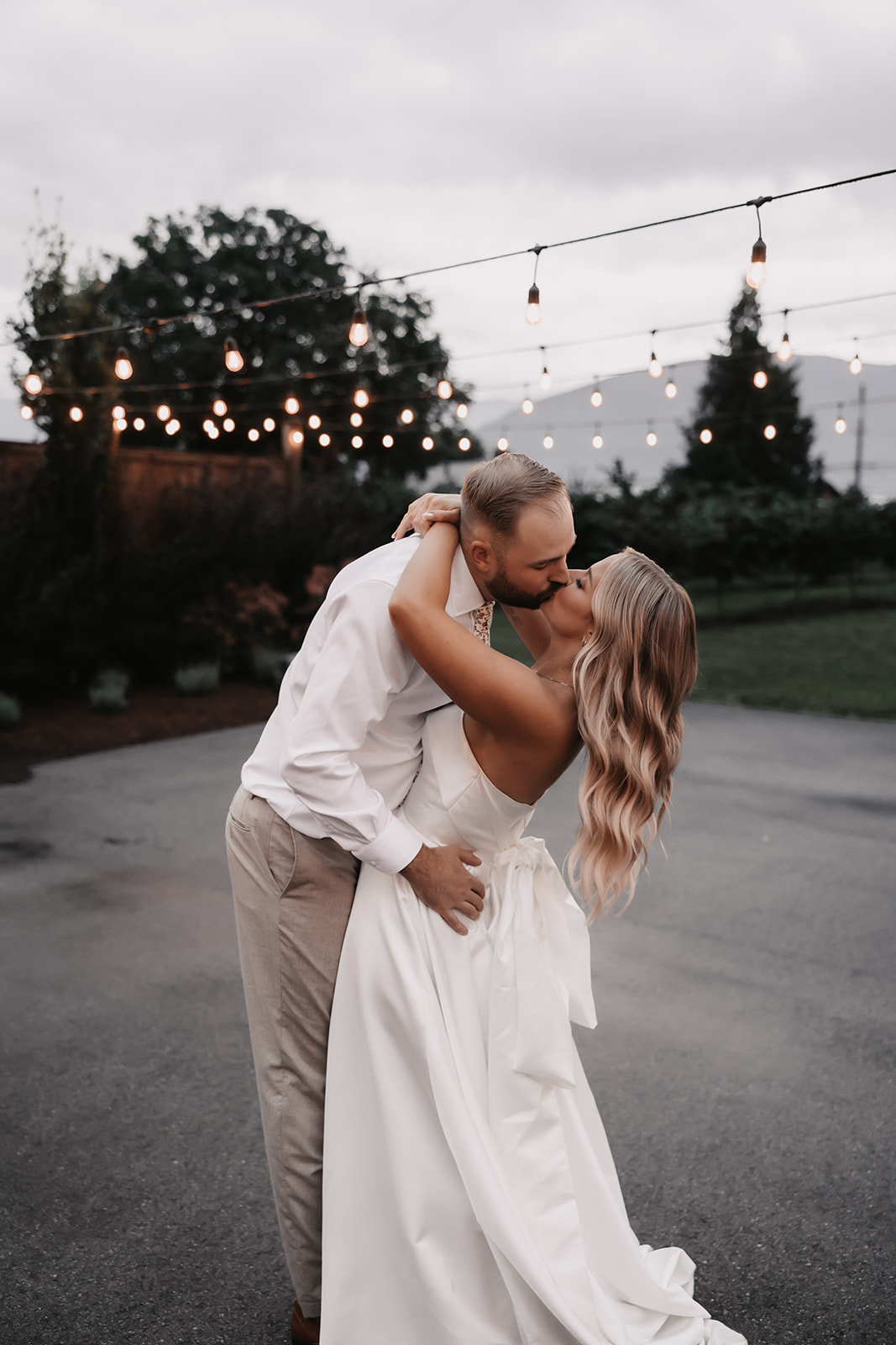 Bride and groom kissing outside with twinkling lights in the backdrop