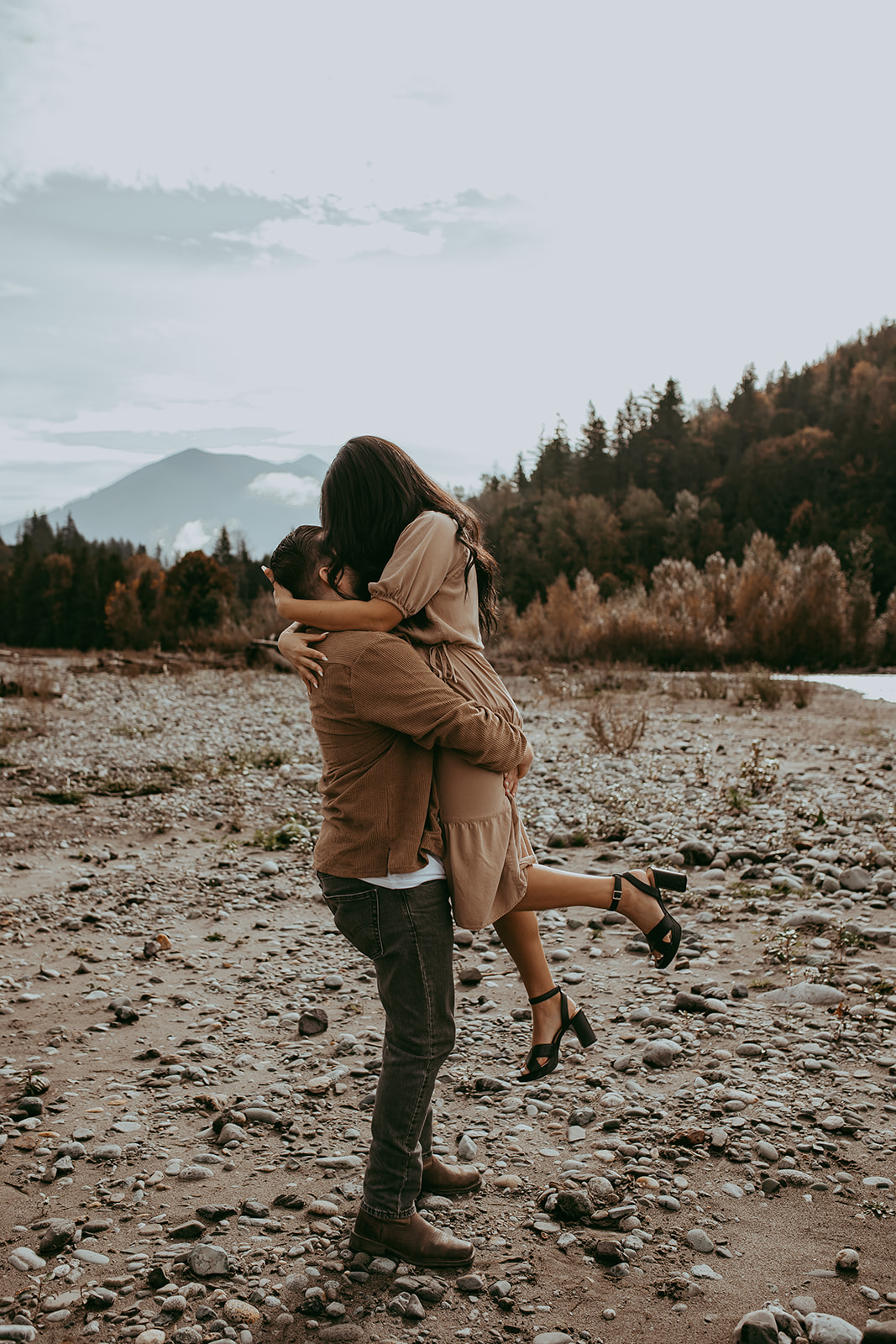 Close-up of a couple sharing an intimate kiss during their engagement session in nature, with a scenic backdrop of trees and mountains.