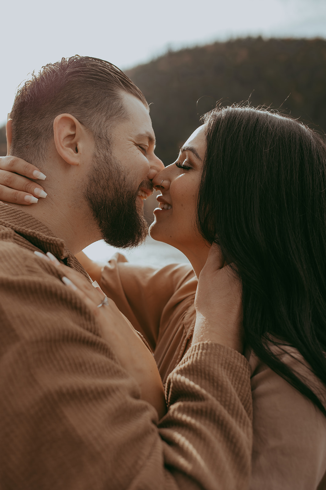 Close-up of a couple sharing an intimate kiss during their engagement session in nature, with a scenic backdrop of trees and mountains.