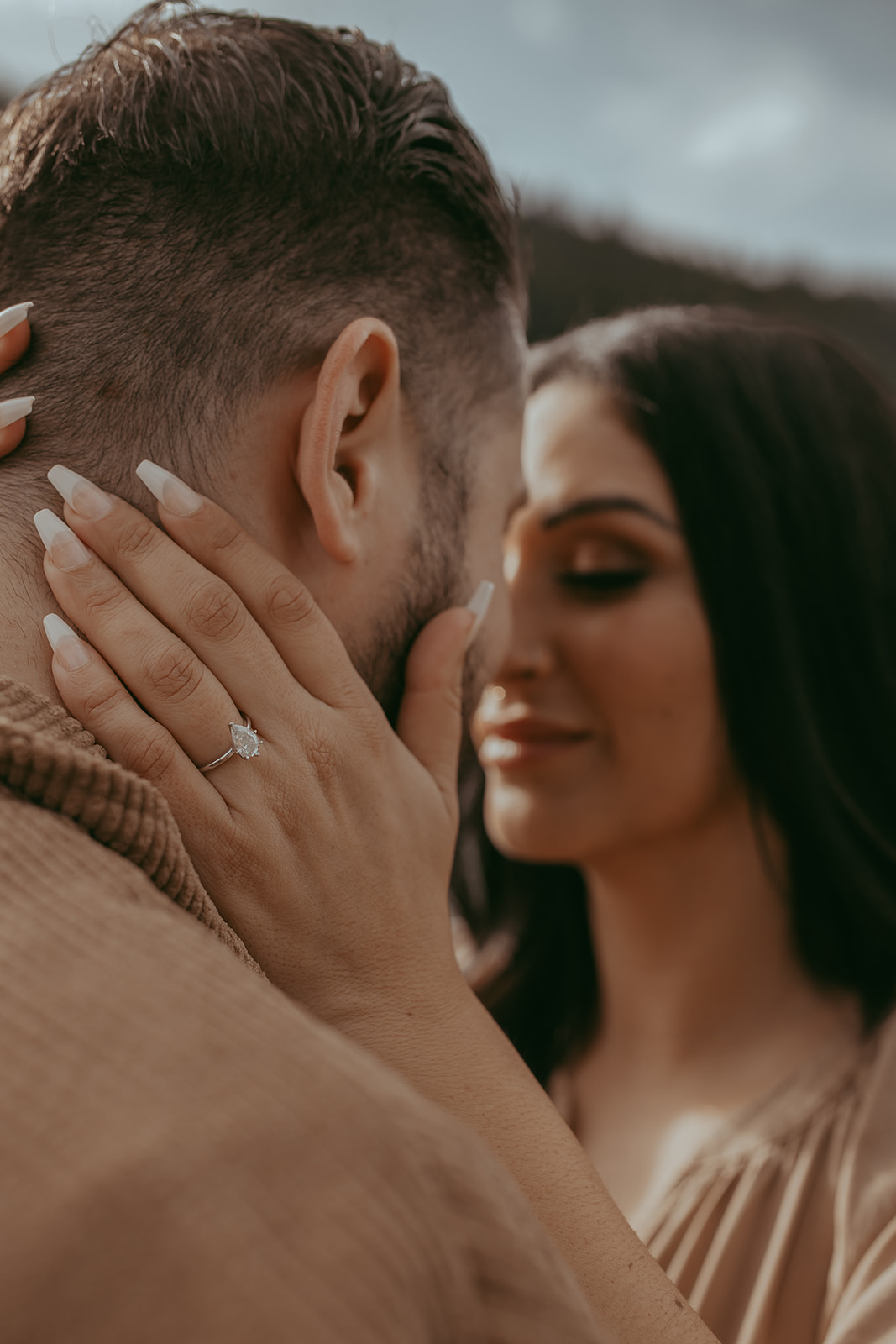 Close-up of a couple during their engagement session in nature, with the woman holding the man's face tenderly while both share a joyful moment.