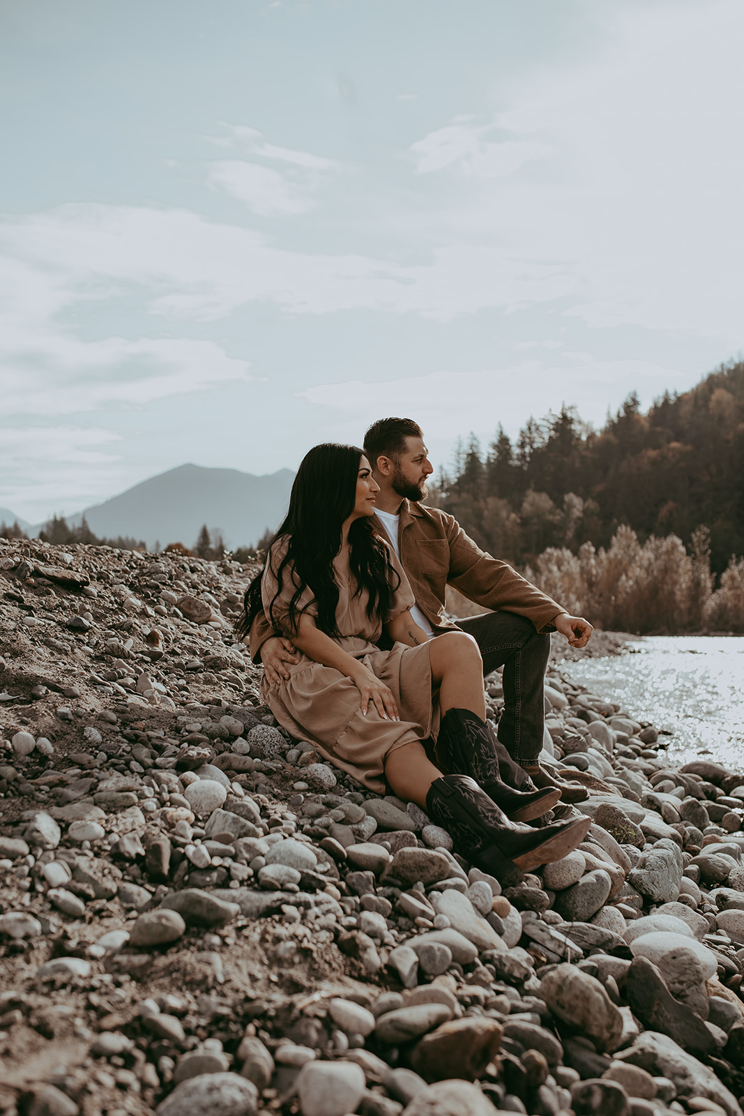 A couple sitting on the rocks at the river during their engagement session, enjoying each other's company with the breathtaking nature surrounding them.