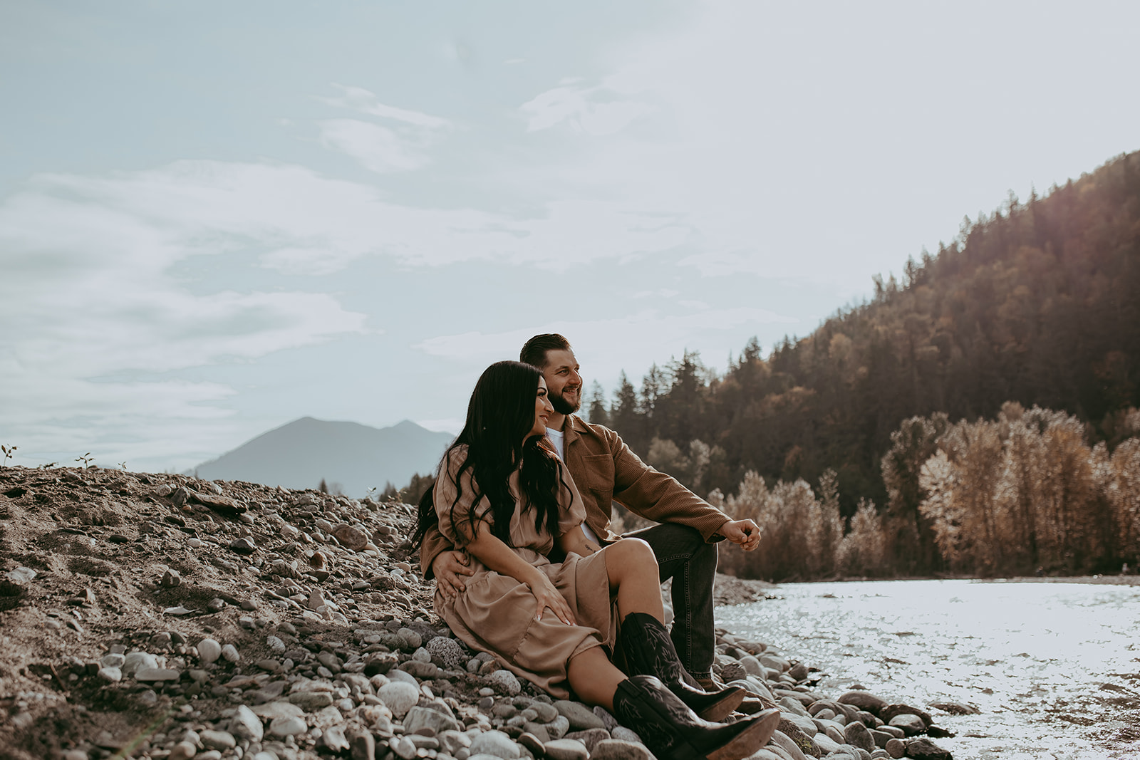 A couple sitting on the rocks at the river during their engagement session, enjoying each other's company with the breathtaking nature surrounding them.