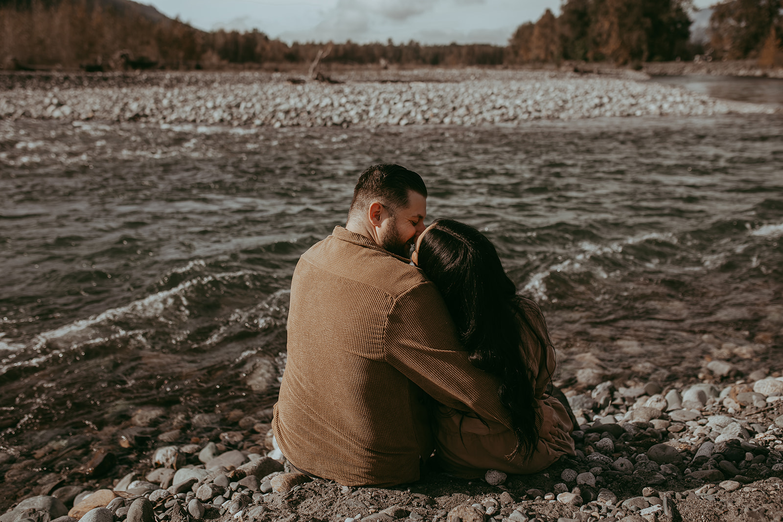 A couple sitting on the rocks at the river during their engagement session, enjoying each other's company with the breathtaking nature surrounding them.