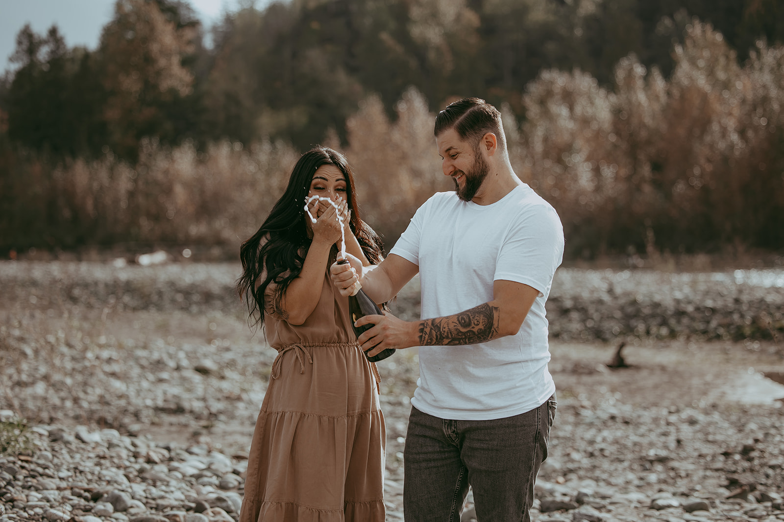 A couple celebrating with champagne during their engagement session, laughing as champagne sprays into the air, capturing a playful and joyful moment.