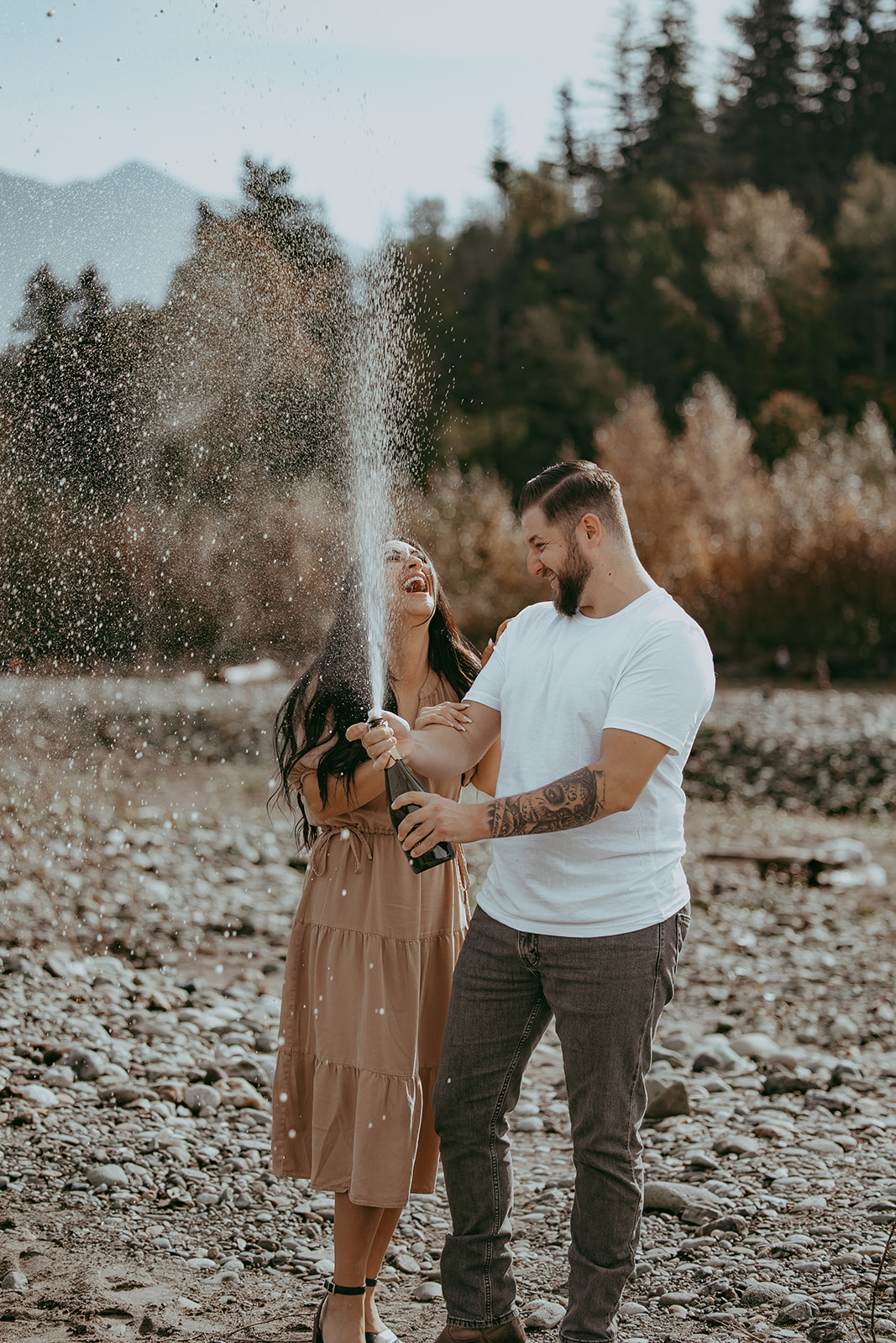 A couple celebrating with champagne during their engagement session, laughing as champagne sprays into the air, capturing a playful and joyful moment.