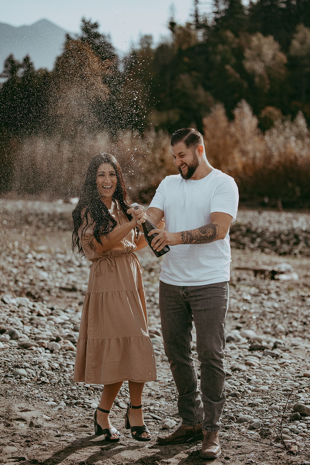 A couple celebrating with champagne during their engagement session, laughing as champagne sprays into the air, capturing a playful and joyful moment.