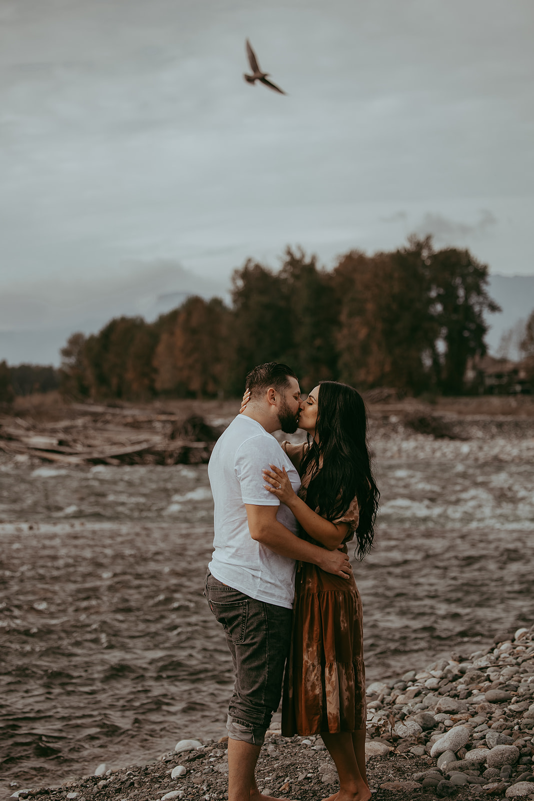 A couple sharing a passionate kiss by the river, surrounded by beautiful nature during their engagement session.