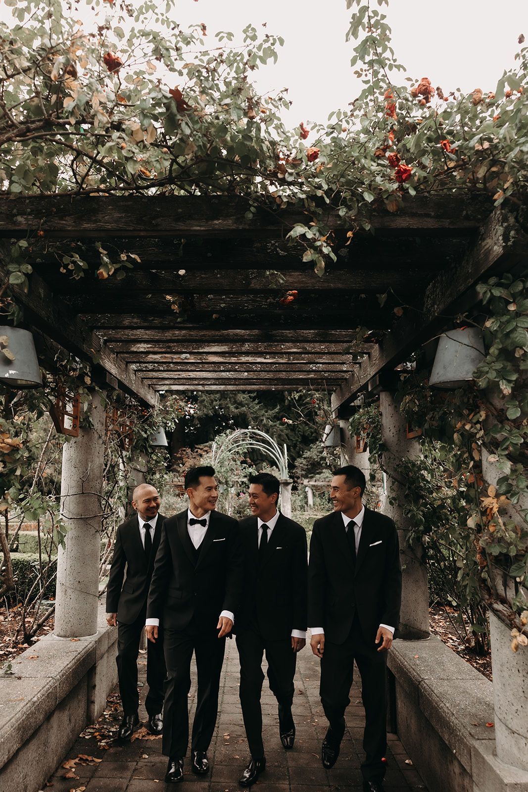 Wedding Day Timeline - Group shot of groomsmen walking through a floral-covered trellis in Vancouver, sharing a light-hearted moment before the ceremony.