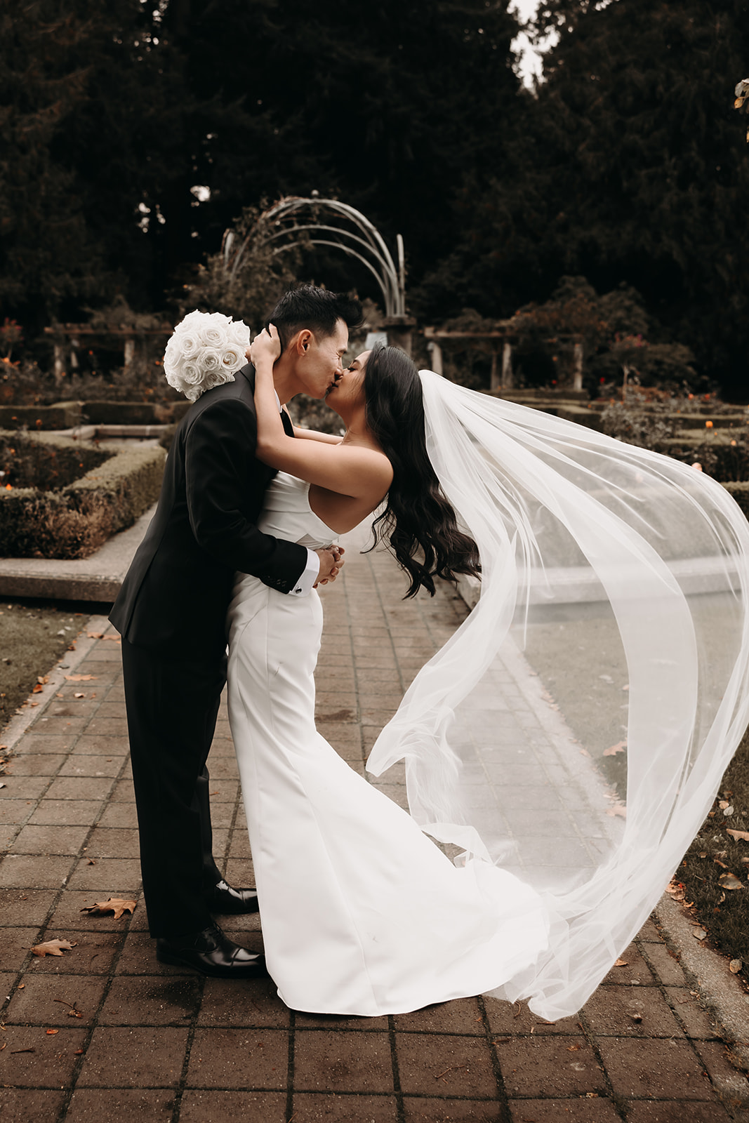 Bride and groom kiss during a tender moment. This image captures the couple sharing a kiss, the wooden pergola overhead providing a beautiful framing element. The wedding day timeline often includes these moments to showcase love in its most pure form.