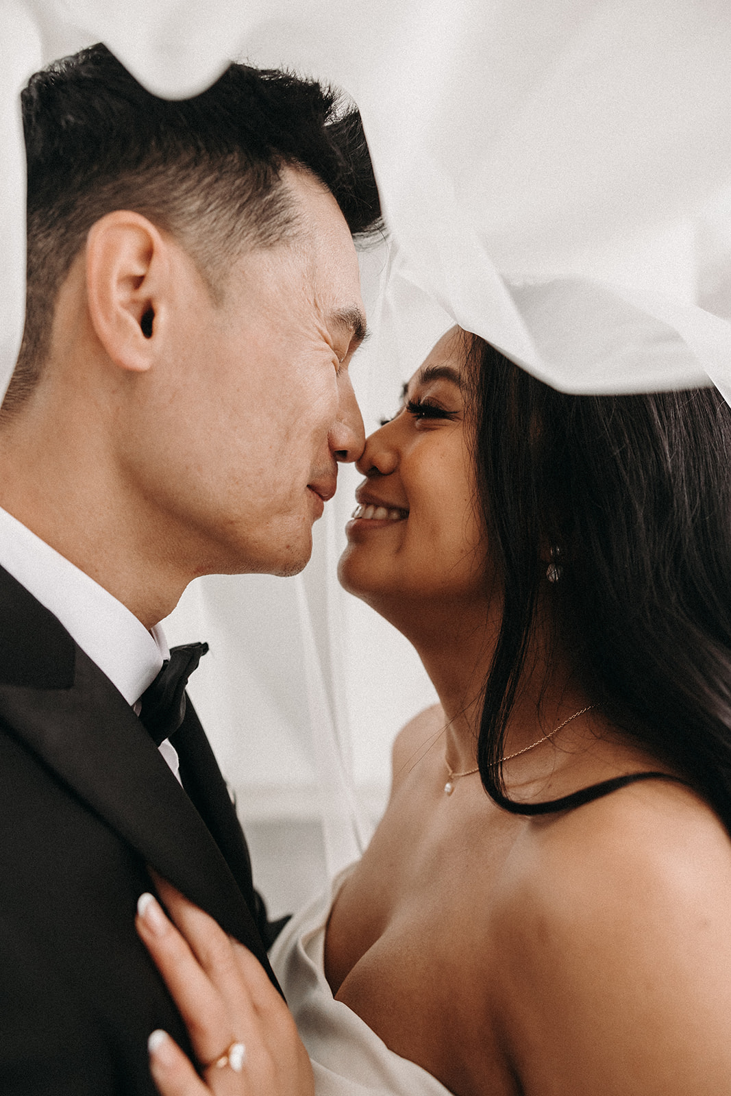 Bride and groom embracing, with the bride’s veil flowing around them as they hold each other closely.