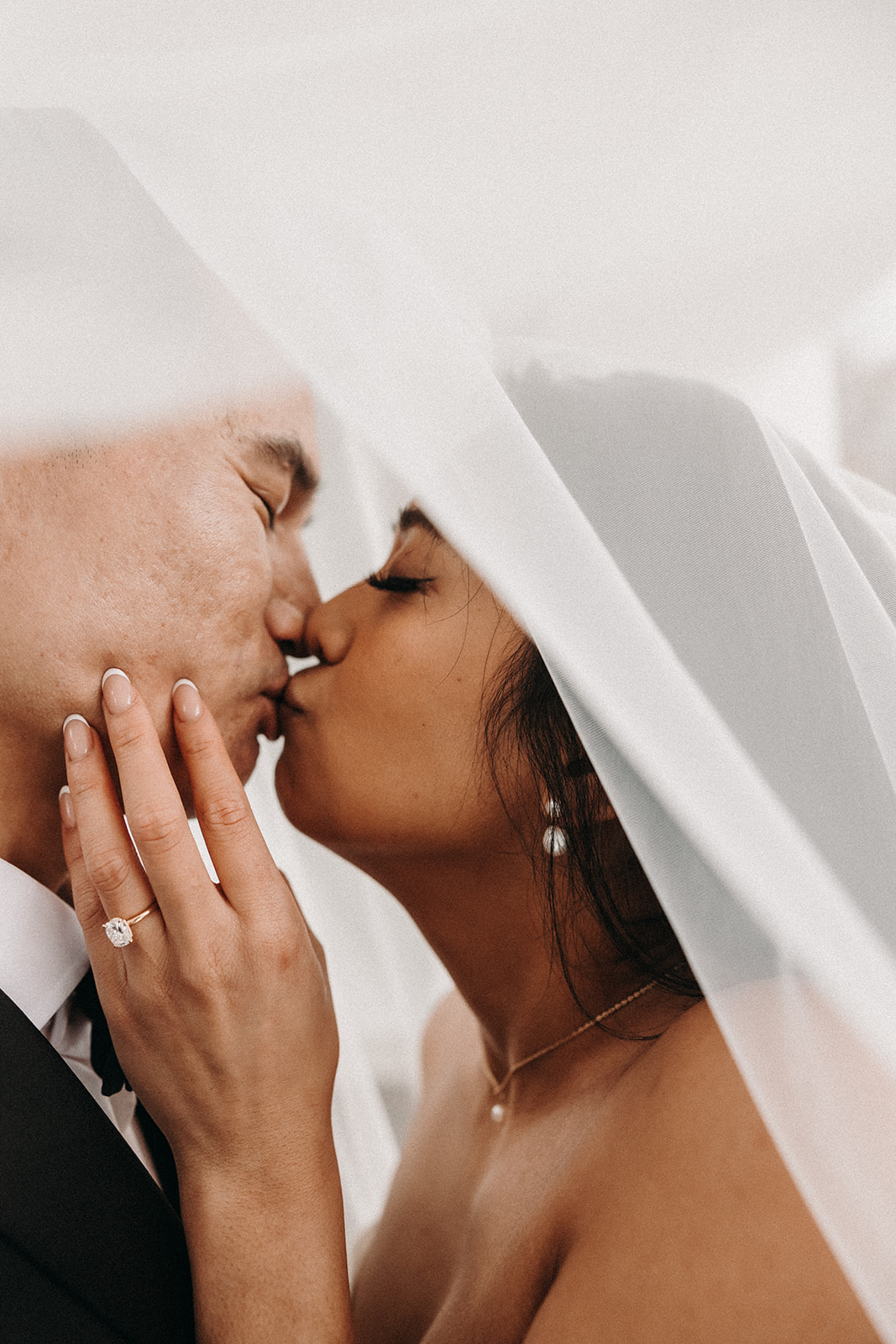 Bride and groom sharing a kiss, with the bride’s veil flowing around them as they hold each other closely.