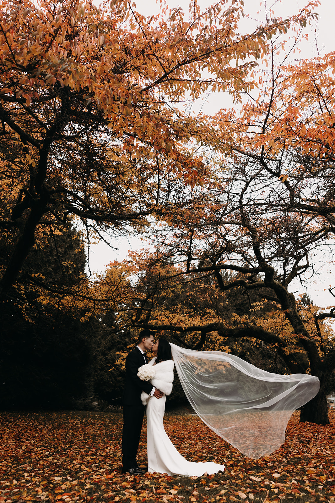 Bride and groom sharing a kiss, with the bride’s veil flowing around them as they hold each other closely.