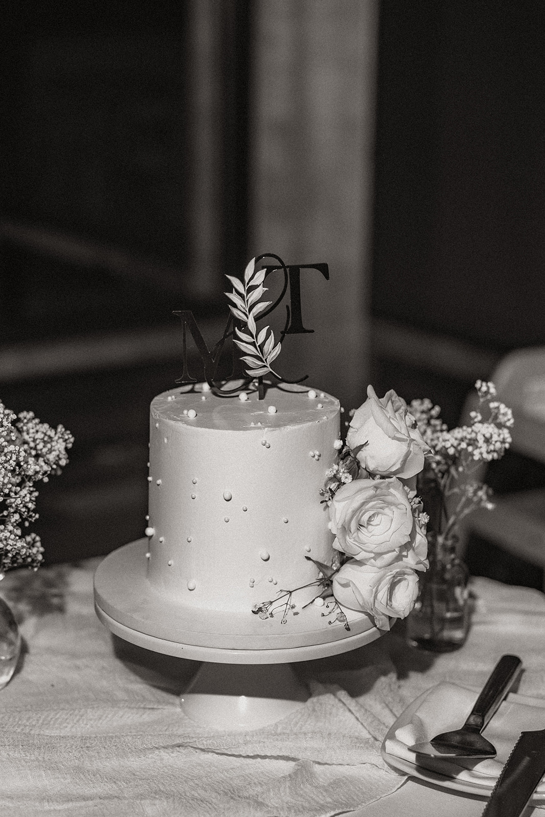 A close-up of the couple's elegant wedding cake decorated with white roses and a custom cake topper featuring their initials. This moment is a beautiful touch in the Wedding Day Timeline