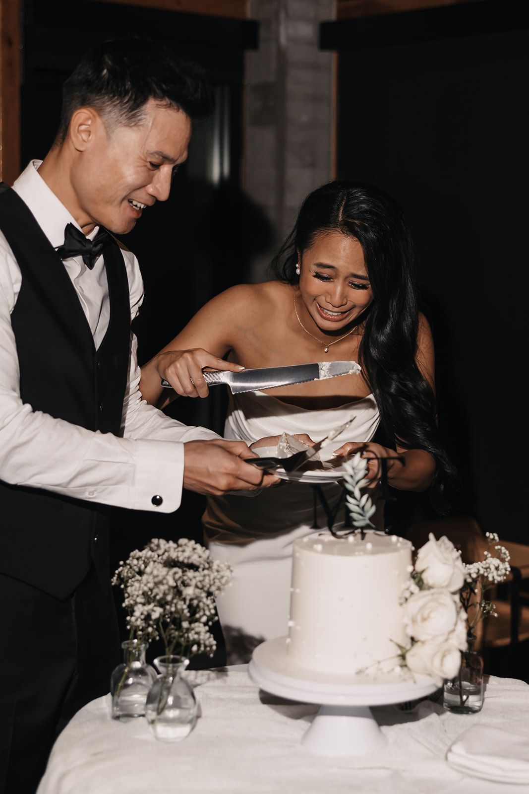 The couple cuts their wedding cake, both smiling and laughing as the bride struggles to cut through the layers. A joyful moment captured during their Wedding Day Timeline.