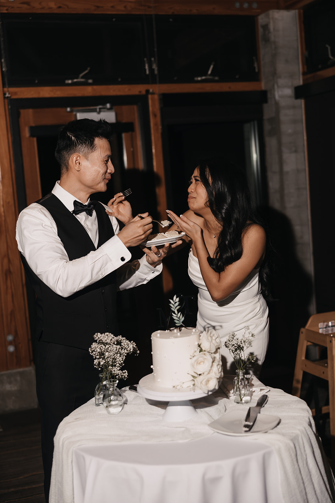 The newlyweds feed each other a bite of cake with playful expressions, embodying fun and intimacy in the final moments of their Wedding Day Timeline.